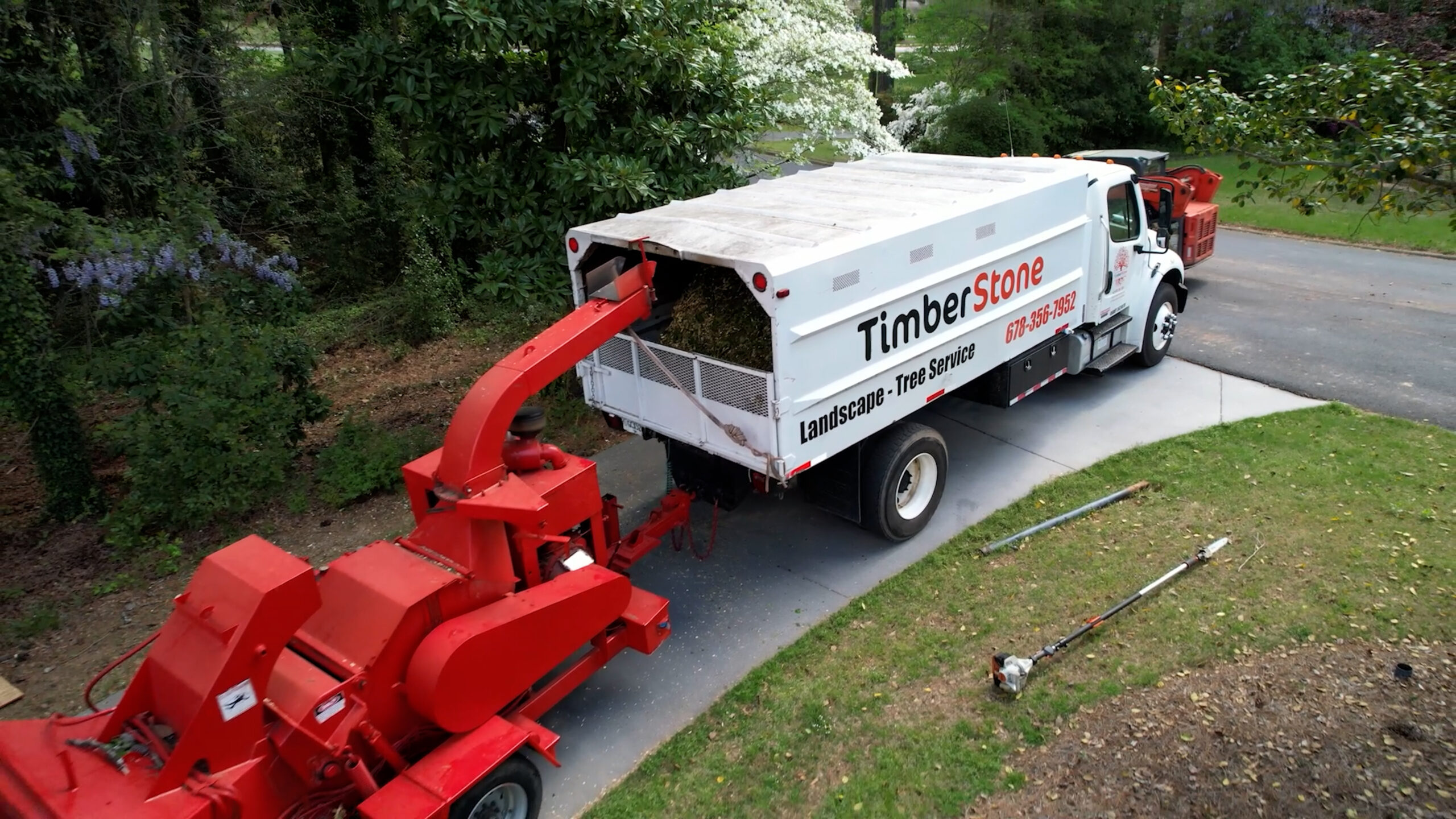 Aerial of the branded Timberstone chip truck and red chipper staged in a driveway under flowering trees