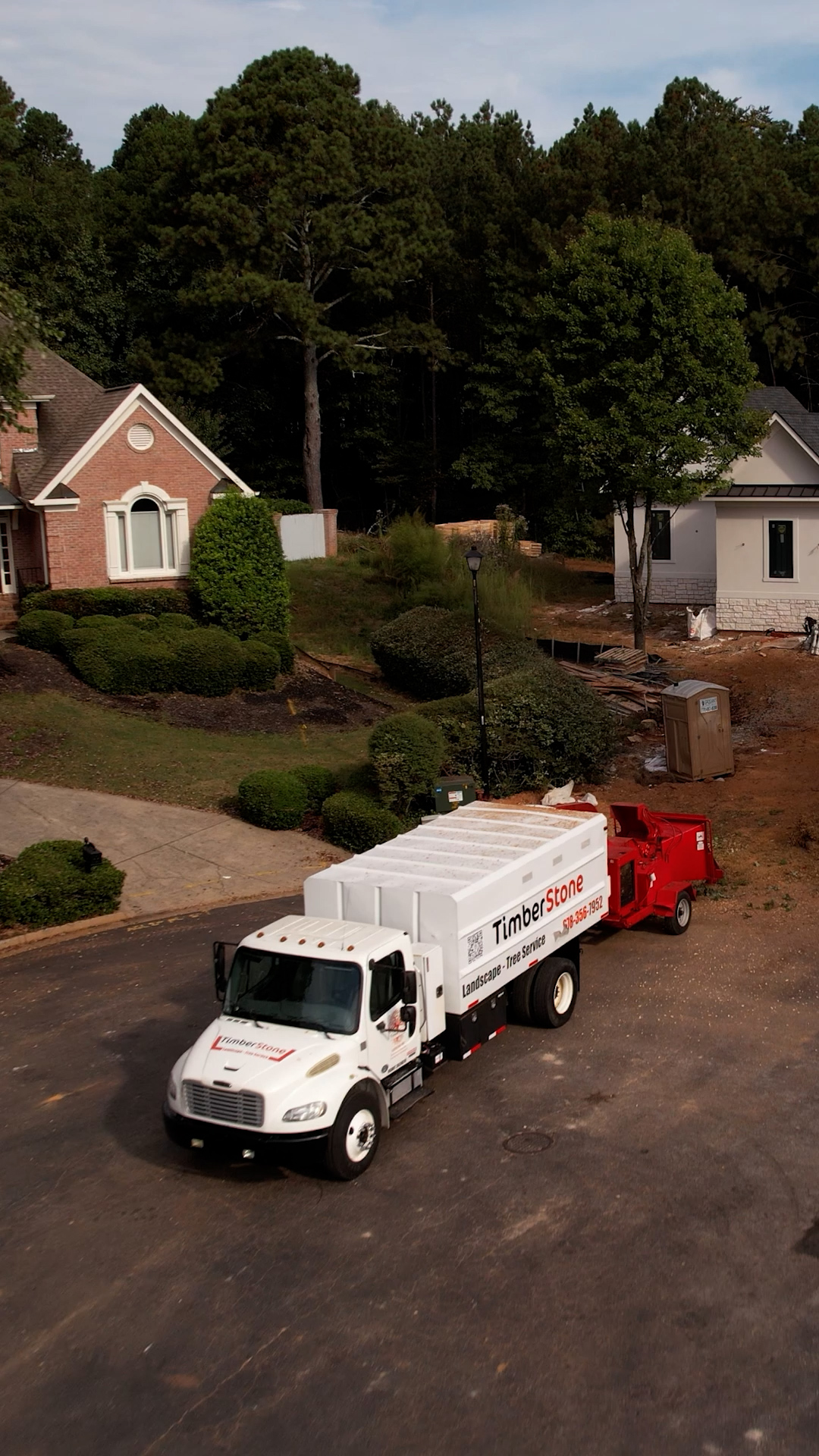 Aerial of the branded Timberstone truck and red chipper parked on a cul-de-sac between an established brick home and a new build